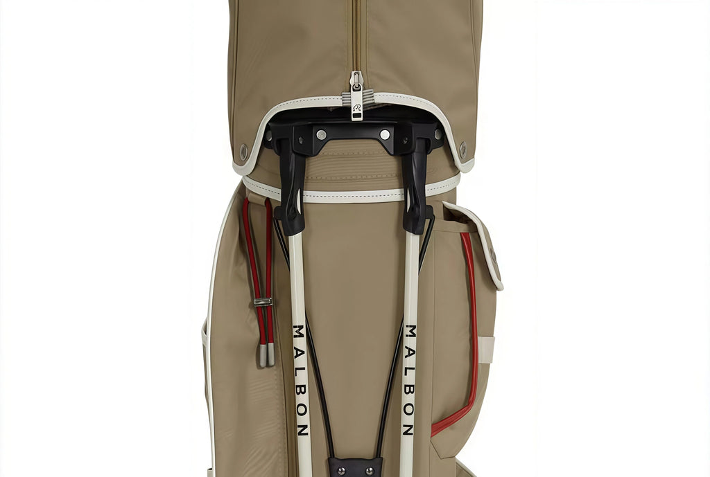 Close-up of Malbon Golf stand bag showing deployed dual stand legs with "MALBON" printed on poles, black support frame, and durable zipper closure.